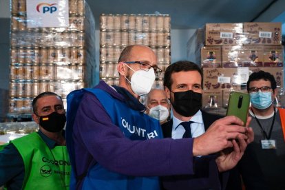 El president del PP, Pablo Casado, consultant el telèfon mòbil d'un voluntari del Banc d'Aliments de Reus.