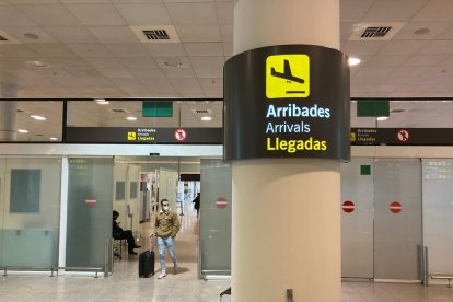 Un senyal de la zona d'Arribades amb un passatger arrossegant una maleta de fons a l'Aeroport del Prat