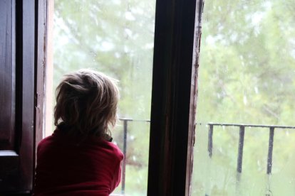 Un niño observa la nieve desde la ventana de su casa.