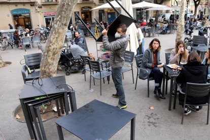 Uno trabajador de un restaurante recogiendo mesas y sillas con gente todavía comiendo.