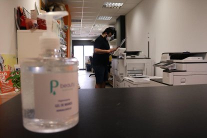 Un empresari autònom d'arts gràfiques treballant amb mascareta, amb una ampolla de gel hidroalcòholic desenfocada en primer pla