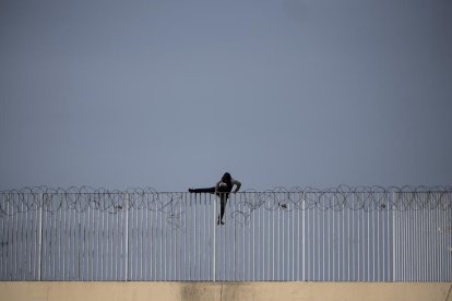 Un menor immigrant no acompanyat intenta saltar una tanca, a Ceuta.