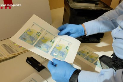 Un agente dels Mossos d'Esquadra sujetando billetes de 20 euros falsificados.