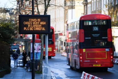 Un bus de Londres passa pel costat d'un cartell que alerta de l'alta incidència de la covid-19 a la capital britànica