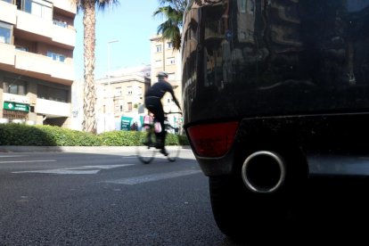 Detall del tub d'escapament d'un cotxe a la Ronda del Mig, i en segon terme una bicicleta passant de llarg.