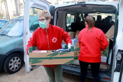 Dos membres de la reu Roja de Tarragona descarregant aliments perpujar-los al pis d'una persona gran al barri dde Sant Salvador.