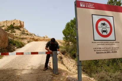 Un cartell del Parc Natural a la Serra del Montsant amb un Agent Rural posant la tanca que en prohibeix l'accés.