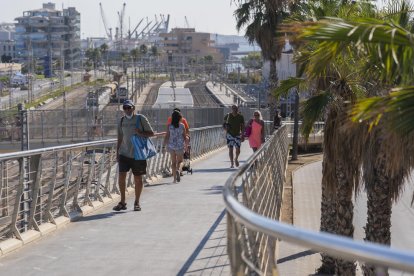 Persones creuant la passarel·la que facilita l'accés des de la Baixada del Toro fins a la platja.