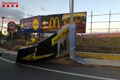 Els Bombers de la Generalitat treballant en la retirada d'un cartell publicitari caigut per la ventada a Valls.