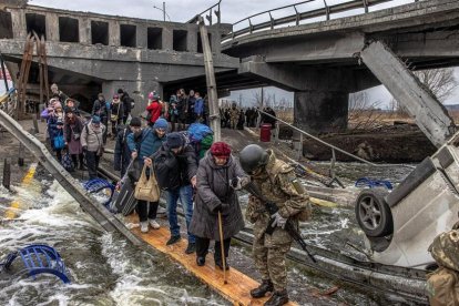 Soldados ucranianos ayudan a la población a superar un puente destruido para acceder a Kyiv.