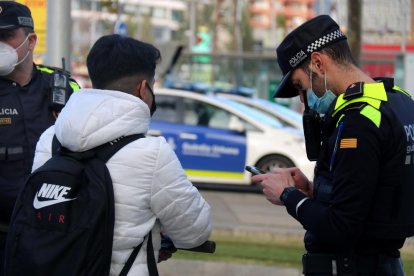 Un usuario de patinete eléctrico, parado durante un control de la Guardia Urbana de Barcelona, ante la Torre Glorias, mientras un agente lo identifica.