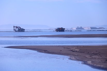 Màquines treballant a la barra del Trabucador amb les salines, al fons.