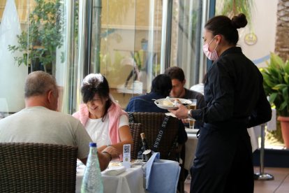 Una camarera sirviendo platos a dos clientes en el restaurante del Hotel Miami de Sant Carles de la Rápita.