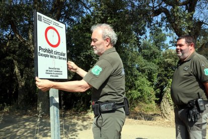 Agents Rurals desplegant un dels cartells que impedeix el pas arran de l'entrada en nivell 3 del Pla Alfa.