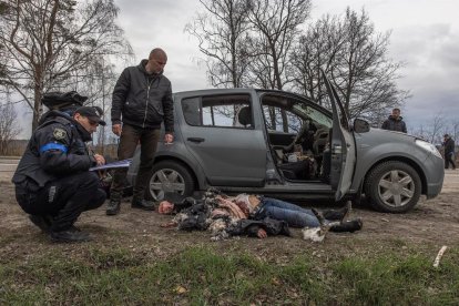 Policies al costat de la dona assassinada estirada a terra al costat d'un cotxe, a Butxa.