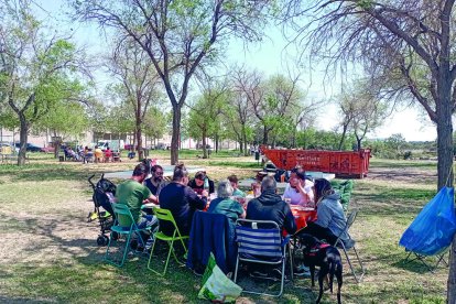 Un grup de familiars dinant al parc per a famílies i al seu darrere el contenidor amb les runes.