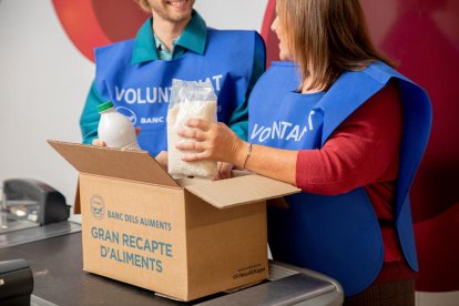 Imatge d'uns voluntaris del Banc dels Aliments guardant un paquet d'arròs i una ampolla de llet en una capsa.