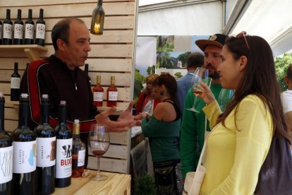 Una chica, con una copa en la mano, escuchando las explicaciones del responsable de una bodega en la Feria del 2019.