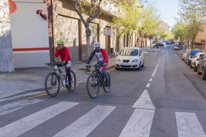 Dos ciclistes i un turisme, sortint de la Mineta des del carrer de Cervantes.