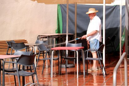 Un home refresca amb una mànega d'aigua la terrassa del local on els avis van a passar la tarda a Vinebre.