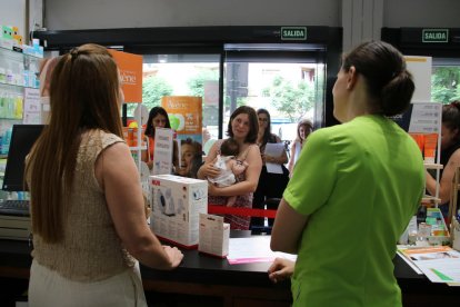 Dos profesionales atendiendo a una madre en una farmacia de Tarragona adherida al servicio de asesoramiento Alletafarma.