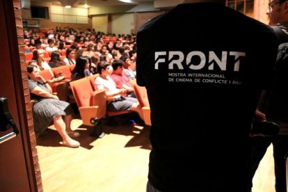 Logo del festival FRONT en la camiseta de un colaborador en las puertas del auditorio de Tortosa con alumnos viendo un documental.