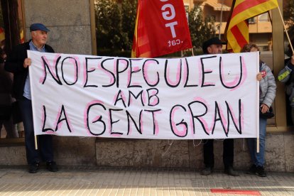 Dues persones subjectant una pancarta durant la concentració que ha tingut lloc aquest divendres davant els serveis territorials de Drets Socials a Tarragona.