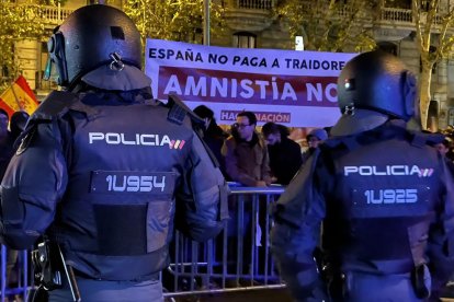 Dos agents de policia custodien la seu del PSOE al carrer Ferraz de Madrid davant de manifestants amb una pancarta contrària a l'amnistia.