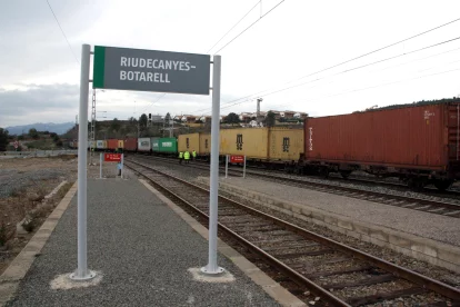 Imatge d'arxiu d'un cartell de l'estació de Riudecanyes-Botarell, en primer terme, amb el tren de mercaderies descarrilat i operaris al fons