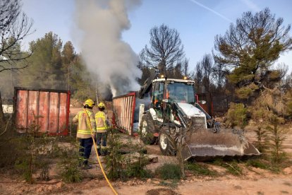 Els bombers treballen amb una retroexcavadora per treure runa que fumejava en un contenidor.