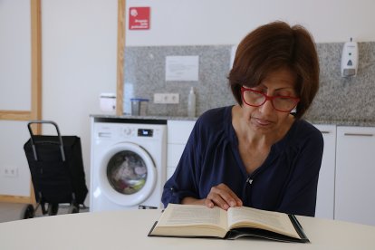 Isabel García, una usuària de Càritas, llegint un llibre mentre espera que acabi la rentadora en un dels punts amb serveis comunitaris de l'entitat