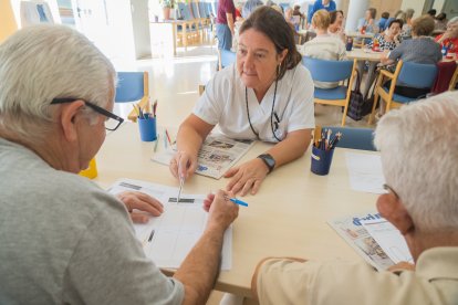 Una membre de l’equip tècnic del programa d’estimulació cognitiva de l’Hospital de Dia Francolí atén a dos usuaris.