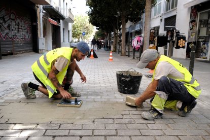 Dos operaris arranjant el paviment d'un carrer de Cambrils.