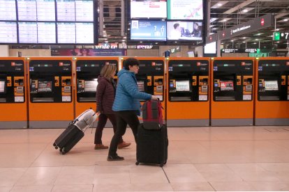Dos personas con maletas por el vestíbulo de la estación de Sants.