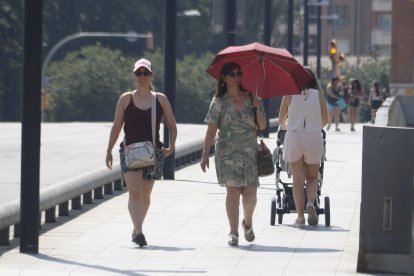 Una dona es protegeix del sol amb un paraigua i una altra amb una gorra, mentre caminen pel pont Vell de Lleida.