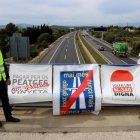 Els portaveus del moviment veïnal 'Mai més peatges', Llorenç Navarro i Enric Lange, mostren les pancartes de l'entitat des de dalt d'un pont sobre l'autopista AP-7 a l'altrua de l'Aldea