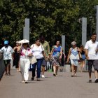 Vianants caminen protegint-se de la calor amb ventalls i gorres.