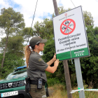 Una agent rural desplegant un cartell que informa sobre el tancament d'un parc natural.