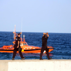 Dos agentes de los Mossos D'Esquadra indicando que se pare el dispositivo de investigación|búsqueda del bañista desaparecido en la playa del Milagro de Tarragona, con una embarcación de Salvamento Marítimo en el fondo.