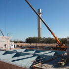 Les obres d'una de les zones de la planta d'ozó a les instal·lacions del CAT de l'Ampolla amb la torre d'aigua al fons i una grua amb els dipòsits en primer terme.