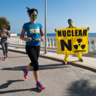 Una chica corre con la cara pintada durante la carrera a l'Ametlla de Mar mientras un chico sostiene una pancarta en contra de las nucleares