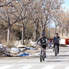 Dos veïns circulen en bicicleta per un dels carrers del polígon, completament envaït per les deixalles i la runa que s'ha abocat il·legalment.