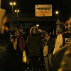 En primer pla, dos conductors d'esquenes esperant. En segon pla, enfocats, els manifestants davant de la policia, al tall de l'A-7 a Tarragona. Imatge del 24 de març de 2018