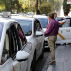 Plano abierto de una hilera de taxis en una parada|puesto de Tarragona, con algunos conductores charlando fuera de los vehículos.