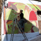 Una de las artistas participantes en la edición 2018 del concurso Riu d'Art de Riba-roja d'Ebre conversando delante de una de las puertas que ha pintado con dibujos inspirado en historias locales.