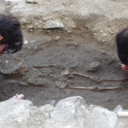 Les restes de l'esquelet d'infant trobat a Romanyà amb dues de les arqueòlogues treballant-hi.