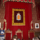 Pla general del saló de plens, amb l'escut municipal presidint-lo, la foto de Quim Torra a l'esquerra i la de Felip VI a la dreta de la imatge.