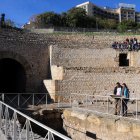 Dos turistes visitant l'amfiteatre romà de Tarragona amb un grup d'escolars assegut a la graderia.