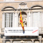 «Libertad presos políticos y exiliados», dice la nueva pancarta con un lazo blanco con una franja roja, en vez del lazo amarillo de la pancarta anterior.