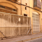 Una gran porta de ferro tapiant un immoble vell que es pretenia ocupar al barri del Carme de Reus, i al fons, un veí del barri, observant.